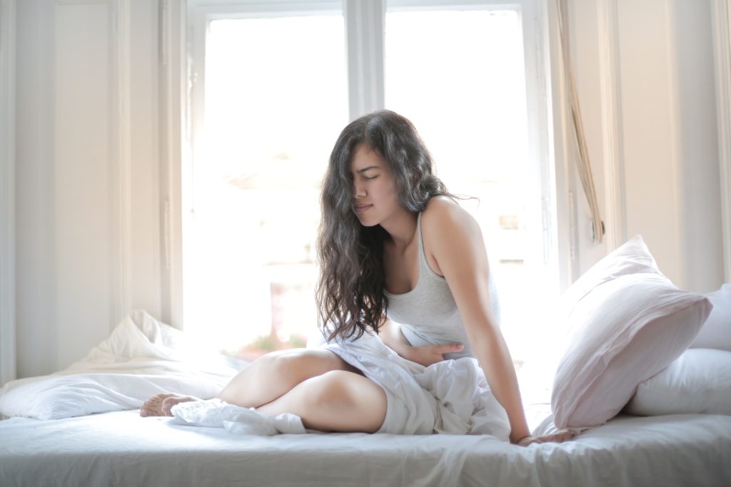 A woman on the bed is holding her stomach and looking in pain.