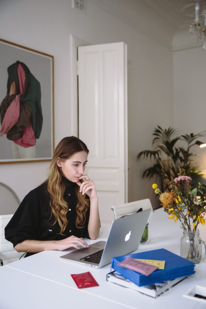 A woman witting on her office desk wearing a black shirt working on her computer.